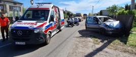 Zdjęcie przedstawia wypadek drogowy z udziałem szarego samochodu osobowego marki Opel, który uderzył przodem w metalowe ogrodzenie i zatrzymał się na trawiastym poboczu. Przednie drzwi od strony kierowcy są otwarte.