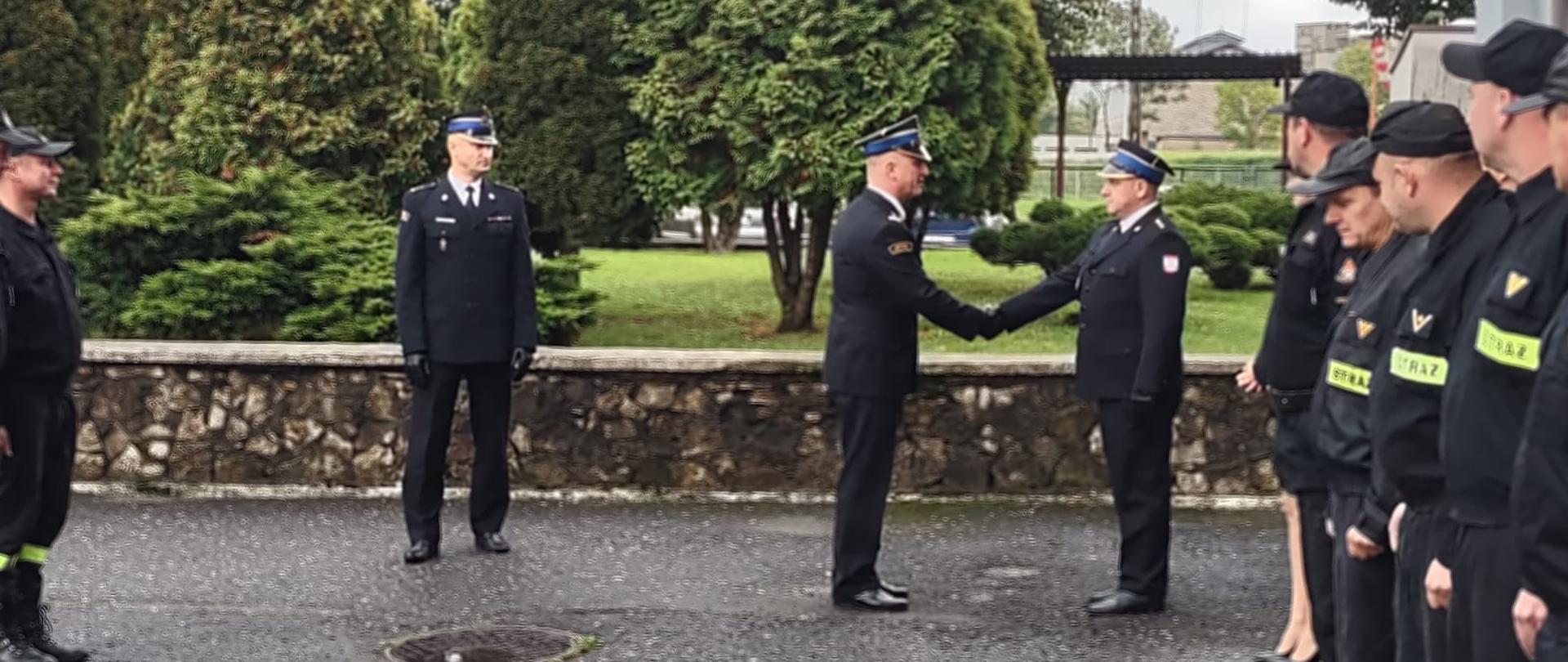 Na zdjęciu znajdują się strażacy ubrani w mundury wyjściowe ustawieni na placu zewnętrznym