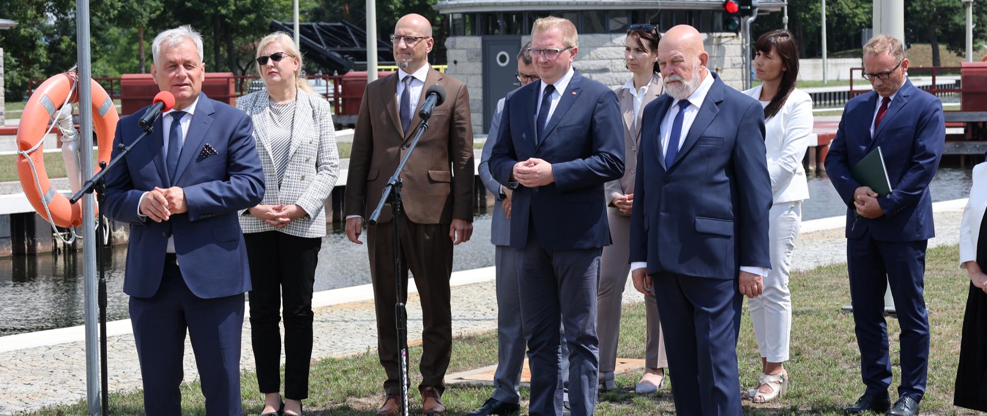 Wojewoda Opolski przed mikrofonem. W drugim planie grupa ludzi. W tle kanał Gliwicki. 