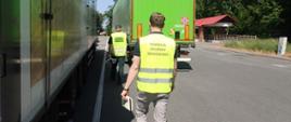 Pracownik Inspekcji Ochrony Środowiska i Służby Celno-Skarbowej idą do zatrzymanego do kontroli pojazdu.