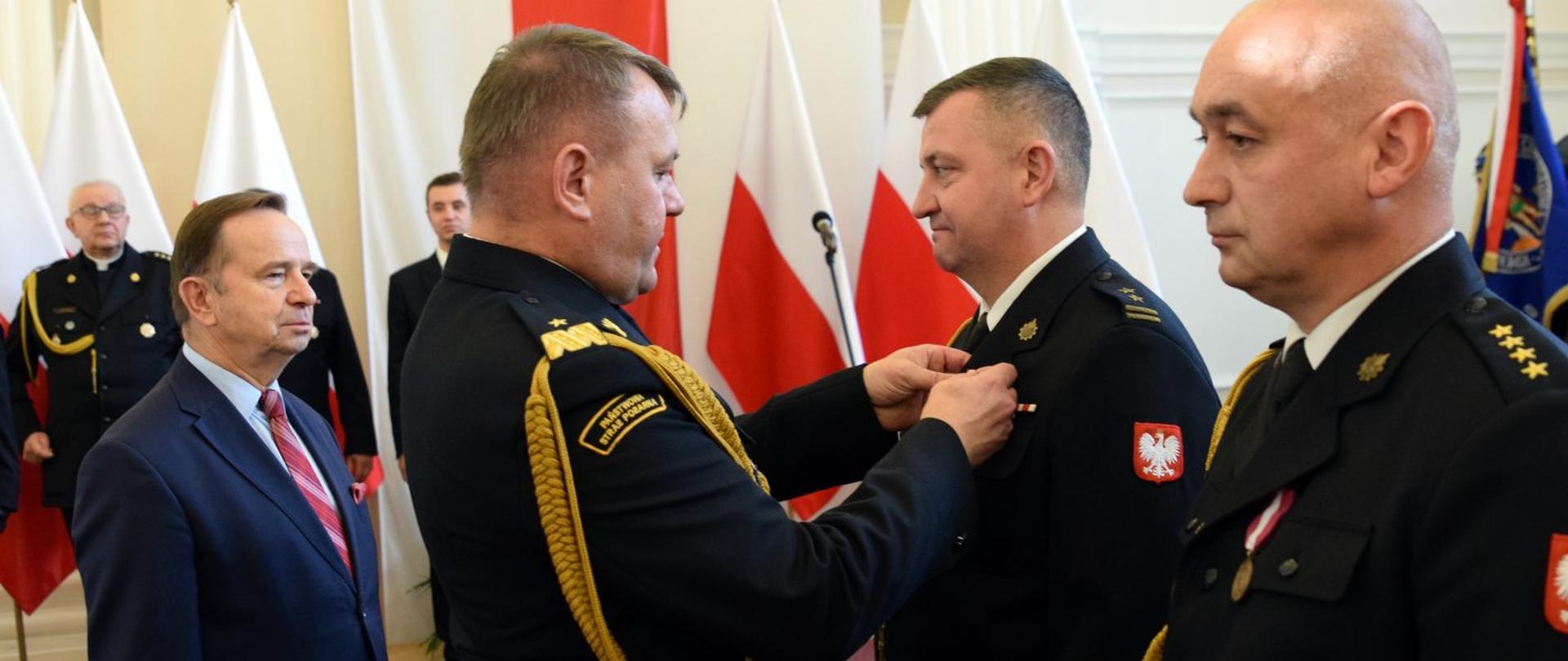 Zdjęcie zrobione w pomieszczeniu. Strażak w mundurze generała gratuluje funkcjonariuszowi awansu.
