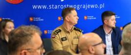 Grajewska konferencja dot. realizacji Programu Ochrony Ludności i Obrony Cywilnej - stół prezydialny przy którym siedzi zastępca podlaskiego komendanta wojewódzkiego PSP, dyrektor WCZK PUW, w tle baner starostwa powiatowego w Grajewie