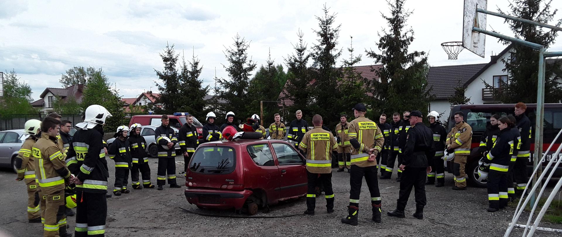 Zdjęcie przedstawia uczestników szkolenia OSP, po środku wrak samochodu, na którym ćwiczone jest ratownictwo techniczne