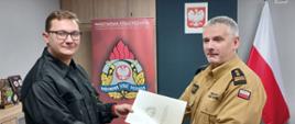 Komendant Powiatowy Państwowej Straży Pożarnej w Człuchowie st. bryg. Radosław Batruch stoi w gabinecie i wręcza akt mianowania na stanowisko dowódcy sekcji st. asp. Łukaszowi Grad.