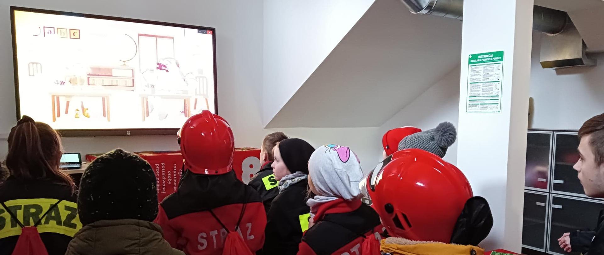 Grupa dzieci podczas oglądania filmów edukacyjnych w sali znajdującej się w budynku straży pożarnej w Pruszczu Gdańskim