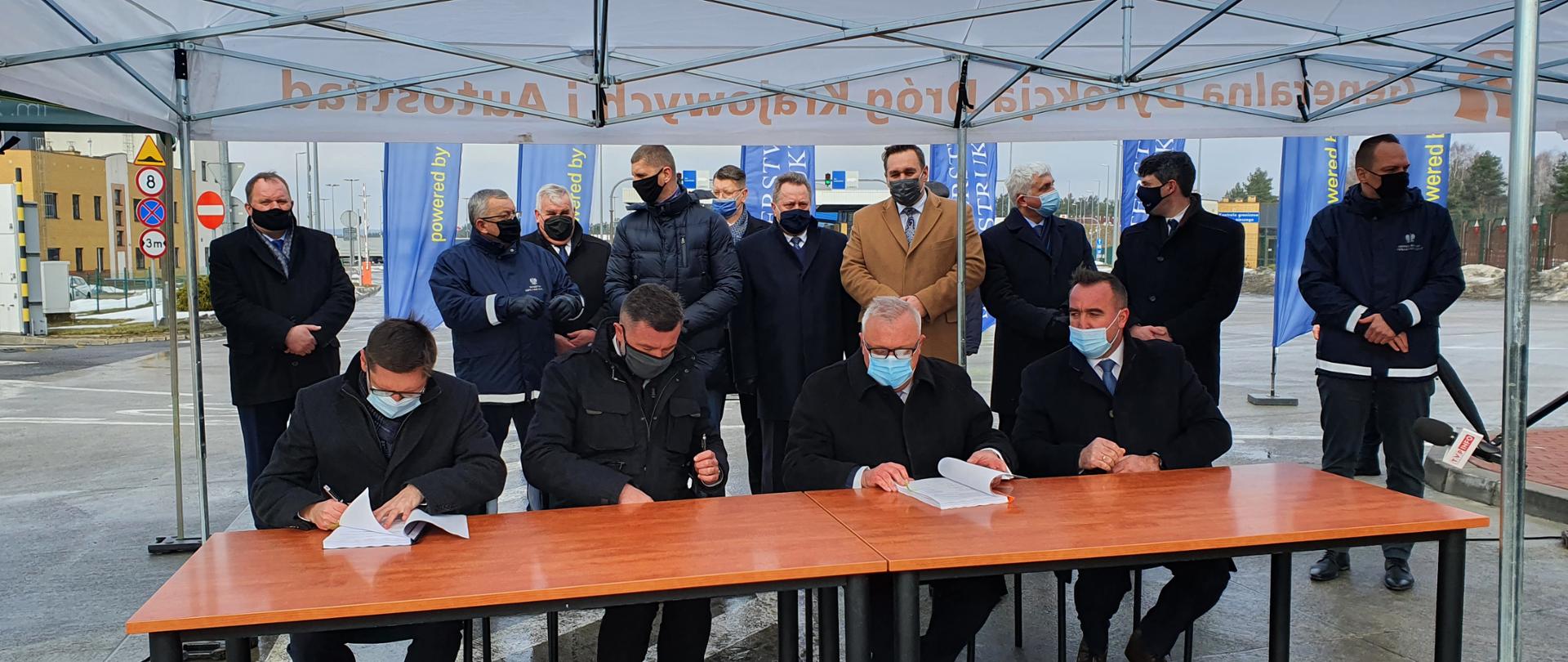 Przy długim stole siedzi 4 mężczyzn, z których 2 podpsuje umowę na projekt i budowę odcinka S19 Kuźnica - Sokółka 