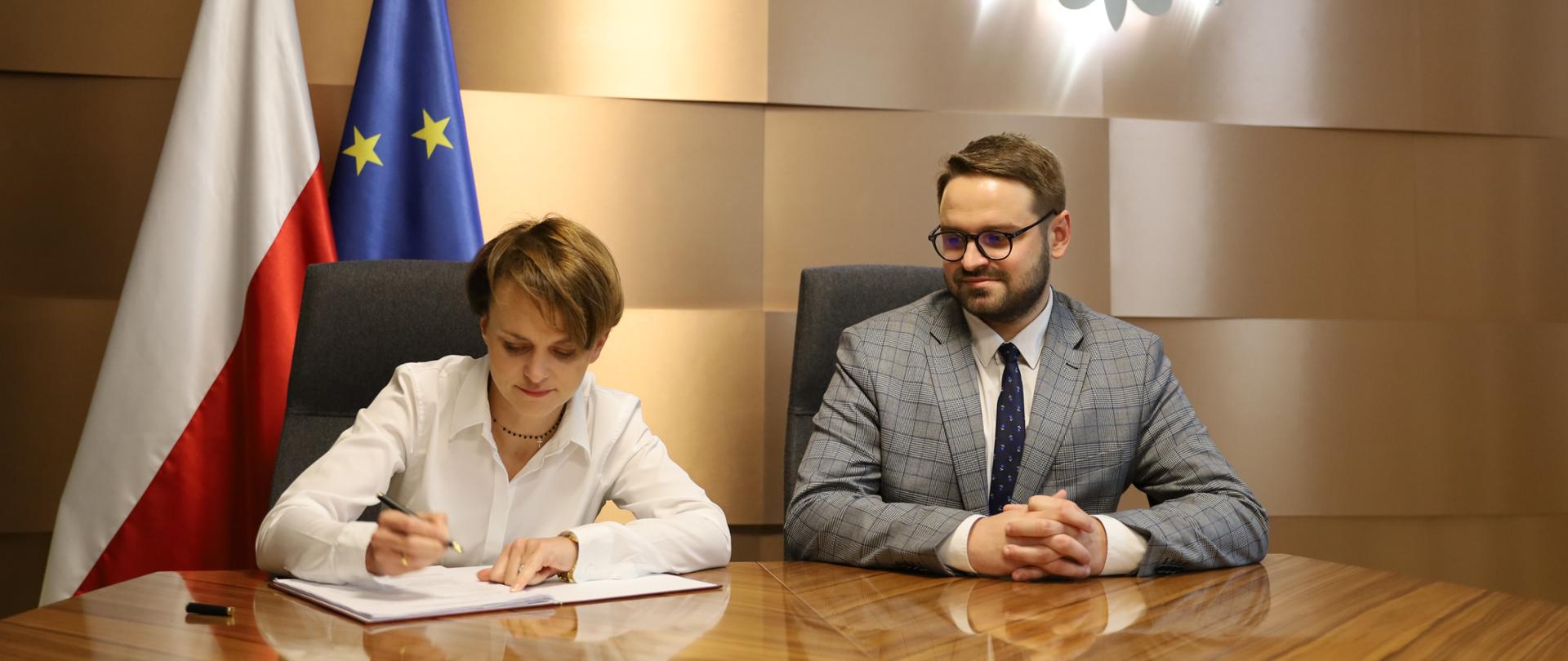 Jadwiga Emilewicz podpisuje porozumienie Stop Smog, obok siedzi Bartłomiej Orzeł.