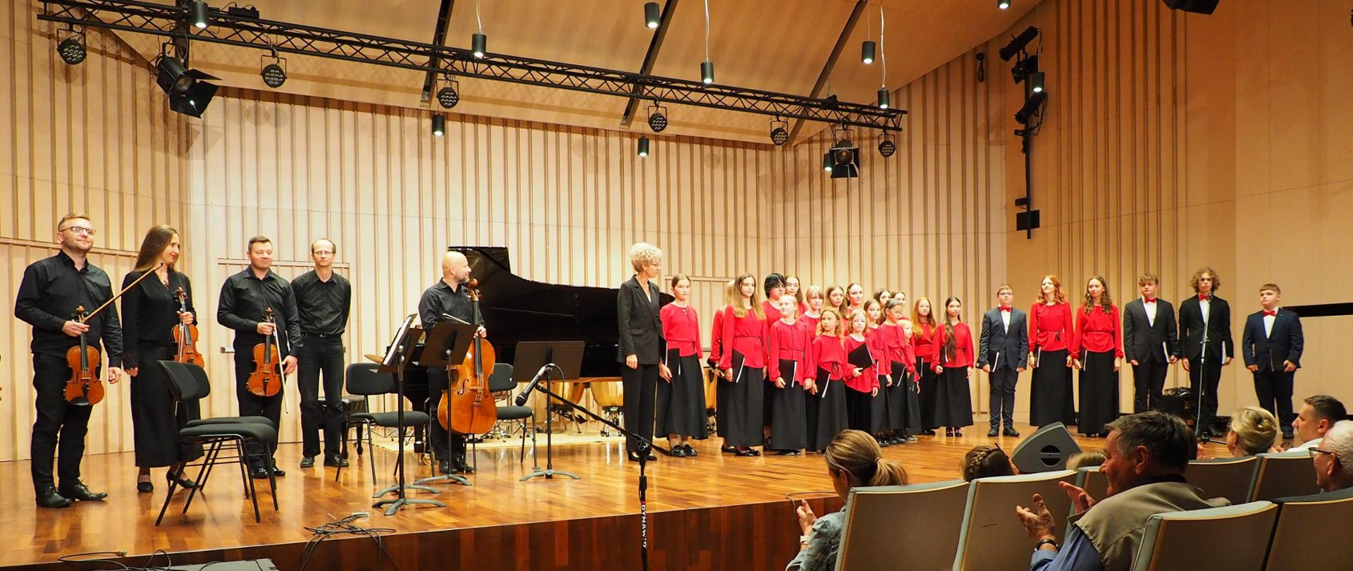 Chór oraz kwintet fortepianowy na scenie w sali koncertowej w budynku.