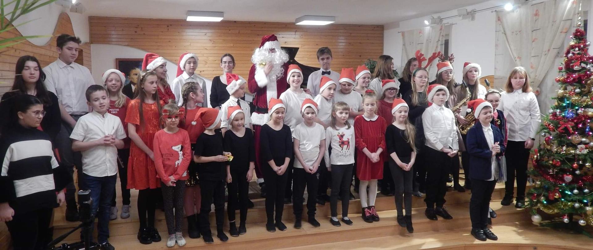 zdjęcie przedstawiające dzieci w czapkach mikołaja na scenie