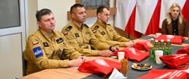 Za stołem siedzą Zastępcy Komendanta Miejskiego PSP w Tarnowie oraz zaproszeni goście, na stole znajdują się torby z logiem PSP z tyłu godło Polski oraz sztandar PSP