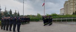 Zdjęcie przedstawia strażaków stojących na palcu przed budynkiem strażnicy podczas uroczystego apelu z okazji Dnia Flagi. 