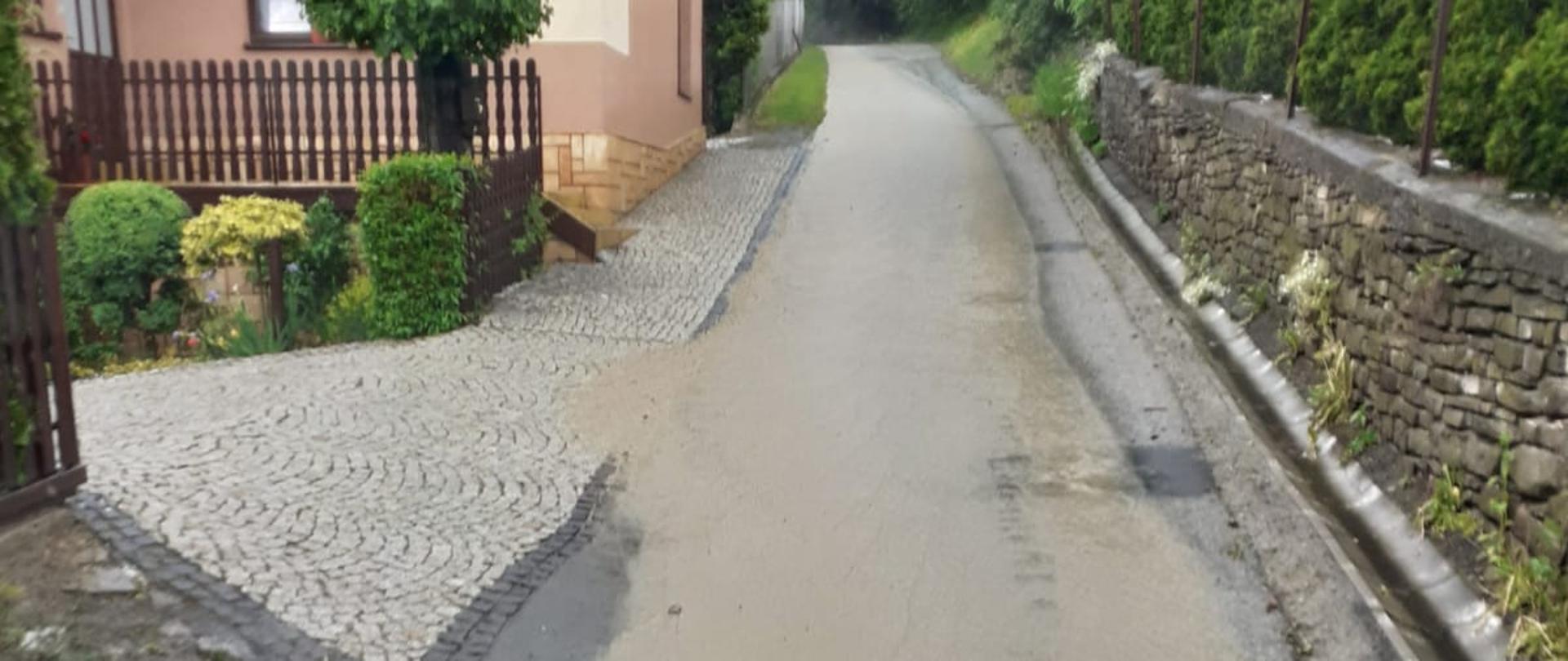 Woda płynie drogą z góry. Obok drogi budynek.