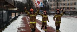Trzej strażacy w biegnący na zaśnieżonej bieżni z podniesionymi rękami. Jeden z nich trzyma flagę 