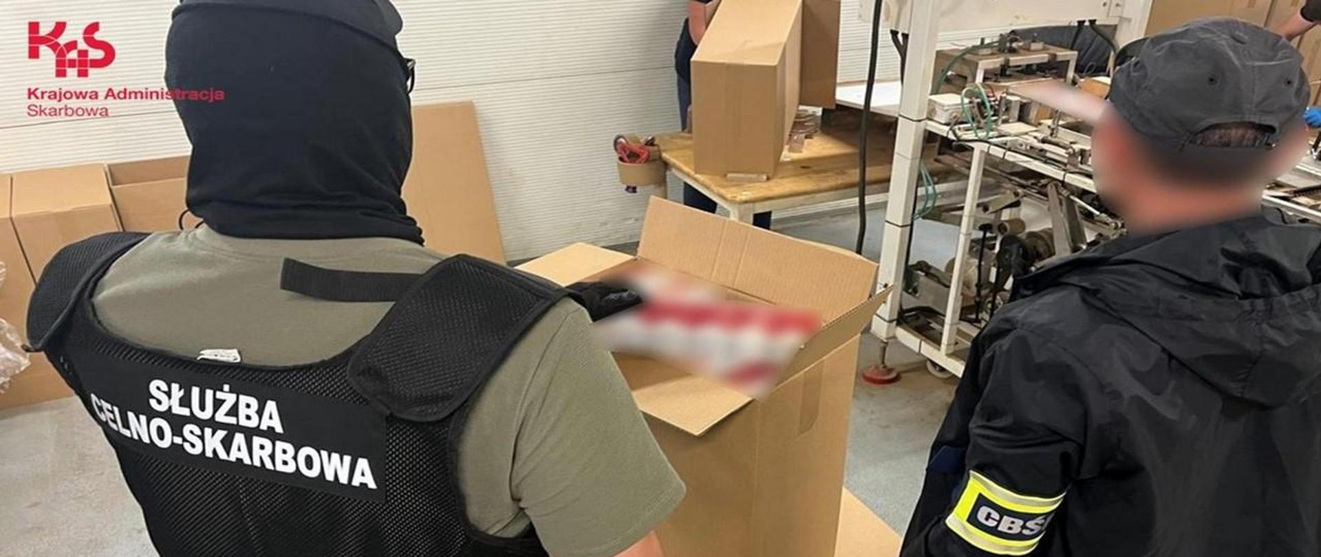 Funkcjonariusz KAS i funkcjonariusz CBŚP stoją przy kartonach z papierosami