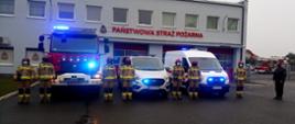 Strażacy stoją pomiędzy otrzymanymi samochodami z włączonymi światłami alarmowymi