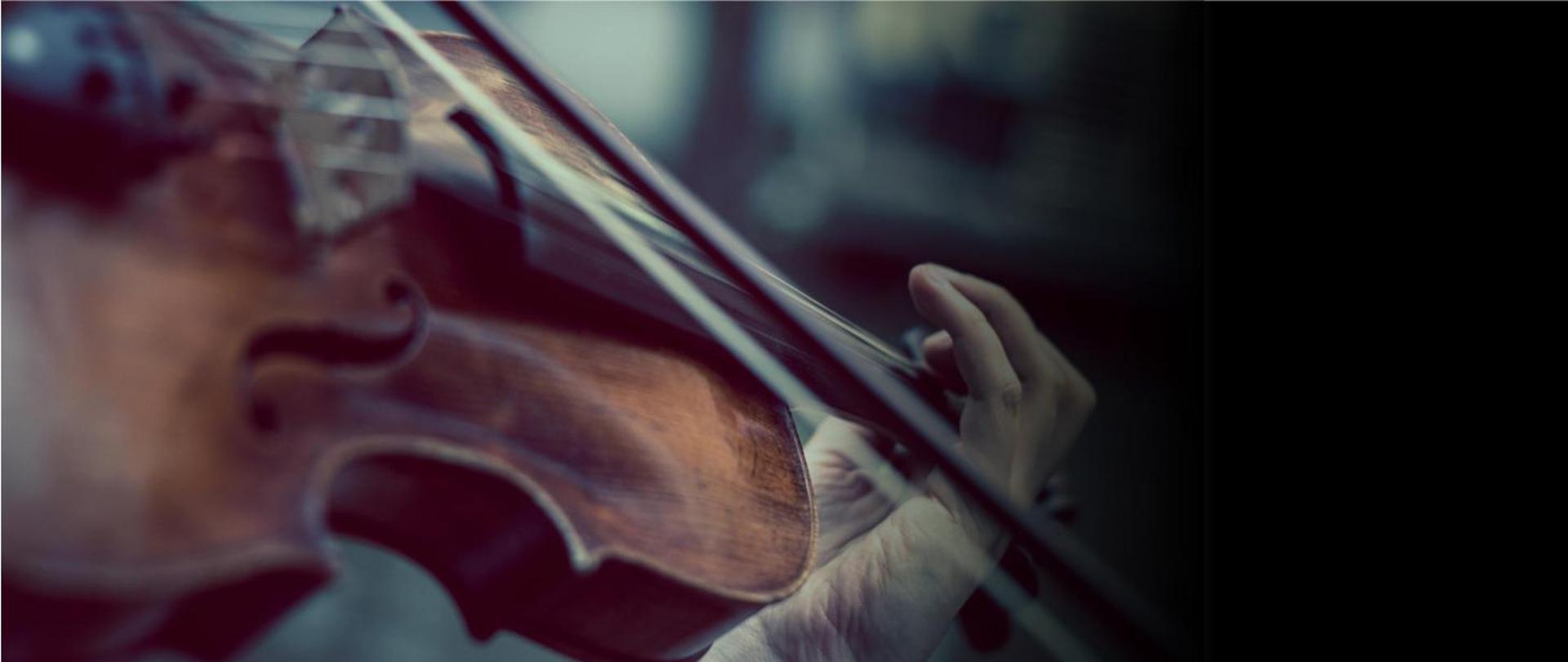 Na ciemnym tle zdjęcie - zbliżenie skrzypiec i dłoni skrzypka