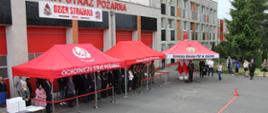 Strażacy i osoby cywilne stoją na placu pod namiotami.