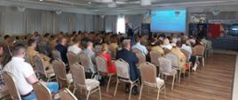 Zdjęcie przedstawia strażaków oraz osoby cywilne podczas seminarium. Osoby siedzą na krzesełkach na sali , natomiast prelegent omawia temat.