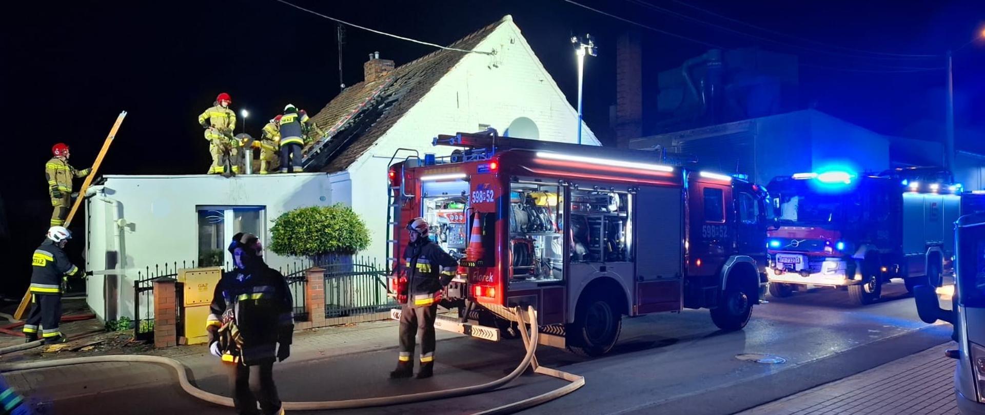 Samochody strażackie na drodze, strażacy na dachu prowadzą działania
