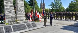 Osoba przemawiająca w obecności żołnierzy wraz z innymi służbami przy pomniku.