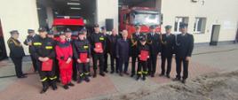 Strażacy Państwowej Straży Pożarnej ochotniczych straży pożarnych zaproszeni goście stoją obok siebie niektórzy trzymają czerwone teczki.
