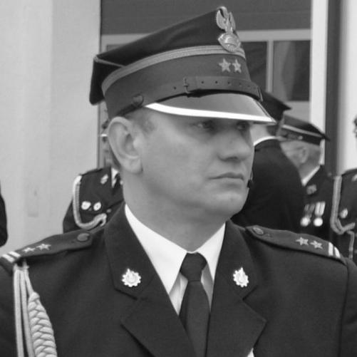 czarno-białe zdjęcie strażaka w okularach, w rogatywce, w mundurze w białej koszuli z krawatem
