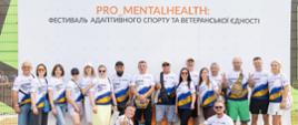 Grupa ludzi pozuje do zdjęcia w koszulkach sportowych pod banerem Pro_MentalHealth