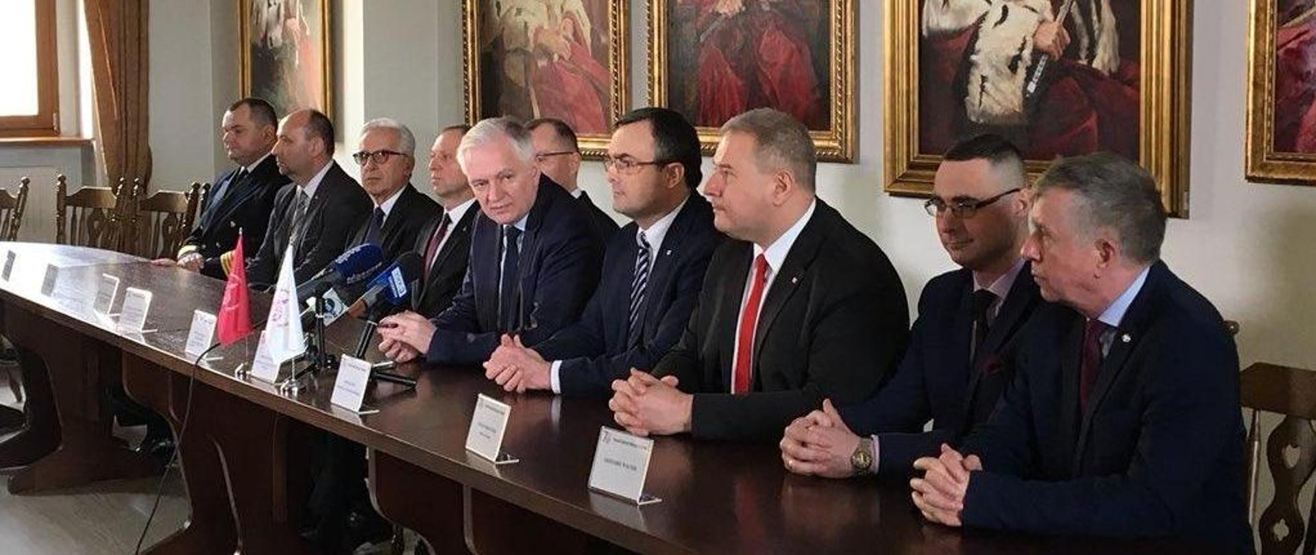 Jarosław Gowin i kadra szczecińskich uczelni siedzą za stołem, przed ścianą z portretami rektorów uczelni