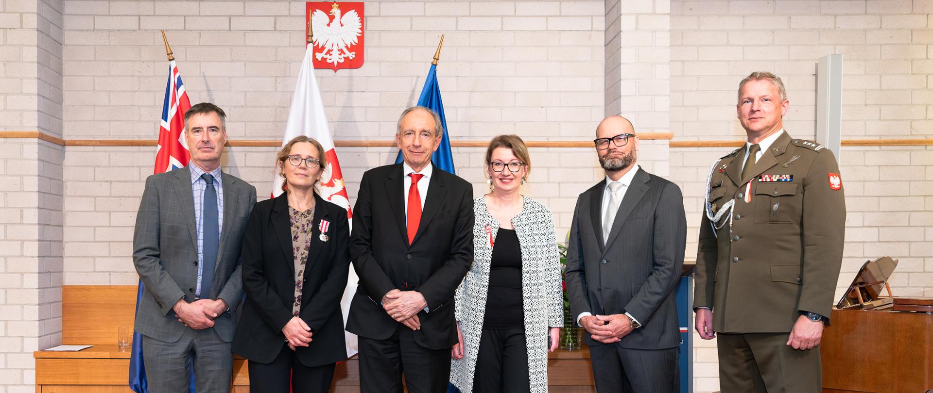 A group of people stands in front of the flags of Australia, Poland and the European Union.
