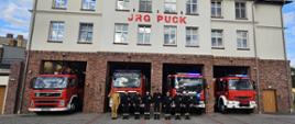 Strażacy ustawieni w szeregu oddają honor tragicznie zmarłemu strażakowi. Za nimi ustawione są pojazdy gaśnicze z Jednostki Ratowniczo Gaśniczej. 