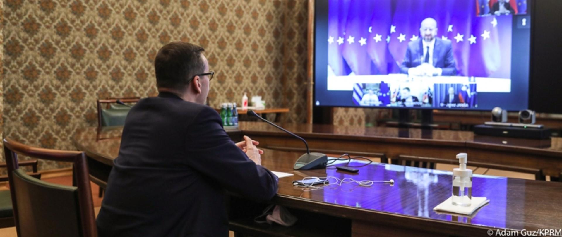 Posiedzenie Rady Europejskiej. Premier Mateusz Morawiecki siedzi za stołem konferencyjnym. Przed nim na ekranie przewodniczący Rady Europejskiej Charles Michel 