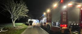 Na zdjęciu widać samochód pożarniczy oświetlający teren akcji. Przed samochodem pożarniczym leży na boku samochód ciężarowy, który tarasuje przejazd DW190