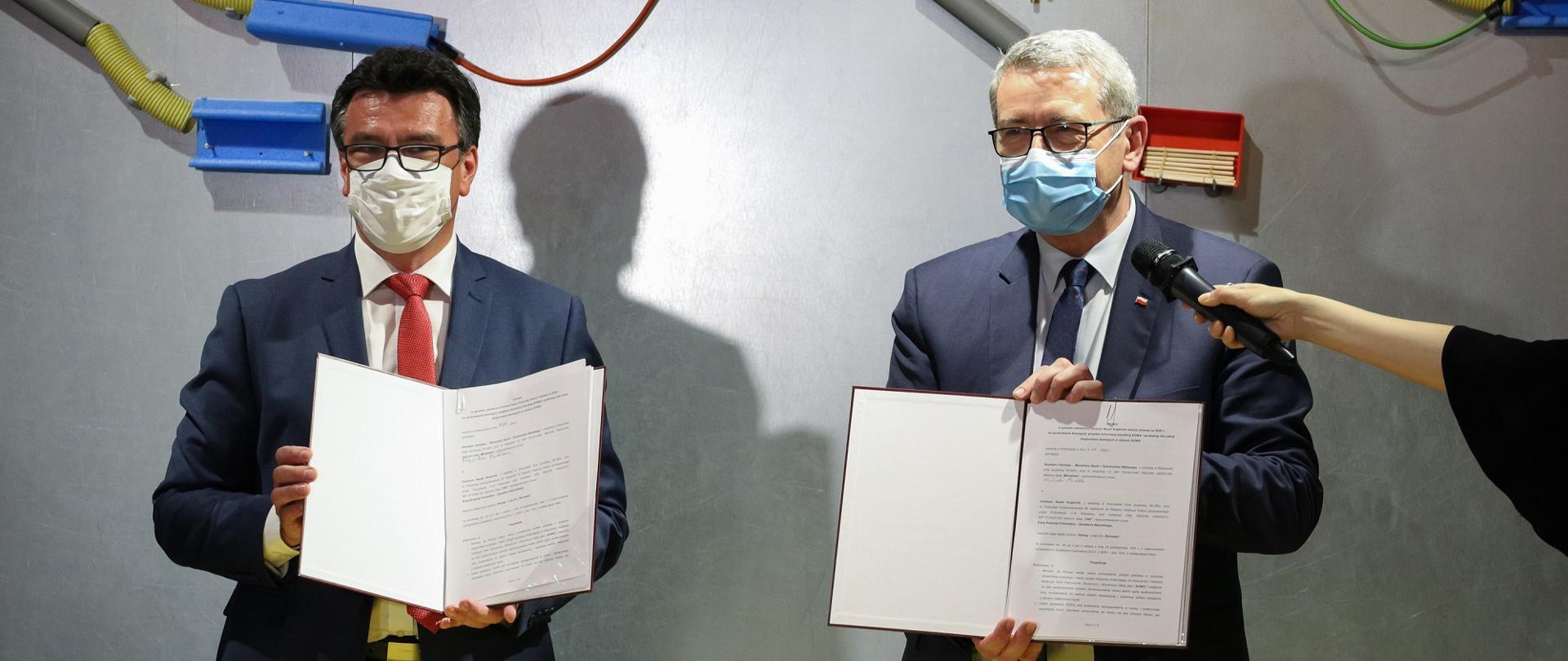 Minister i przedstawiciele CNK stoją prezentując umowy SOWA.