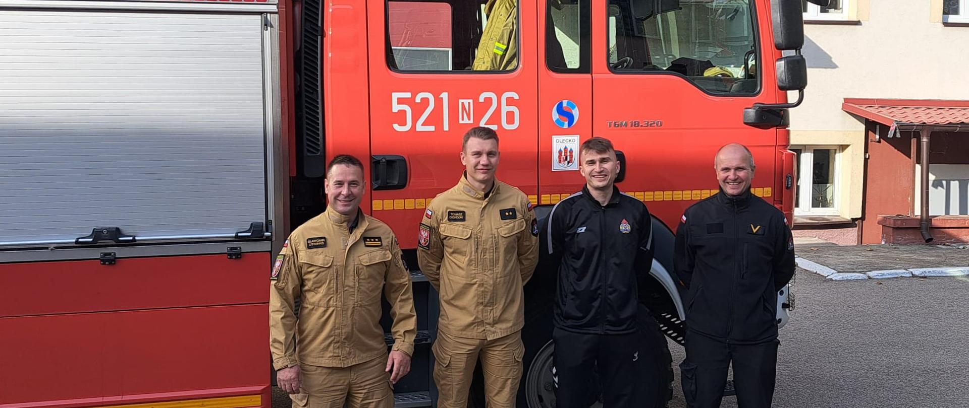 Na zdjęciu widać strażaków na tle wozu strażackiego.
