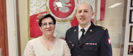 Zdjęcie przedstawia jubilatkę oraz p.o. komendanta na tle sztandaru KP PSP