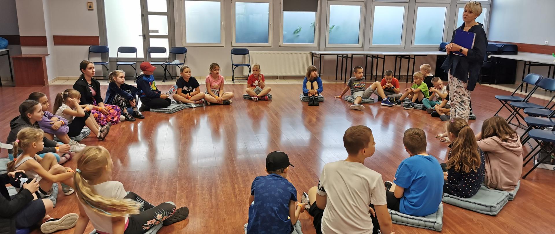 Dzieci siedzą w kręgu i słuchają prelegentki