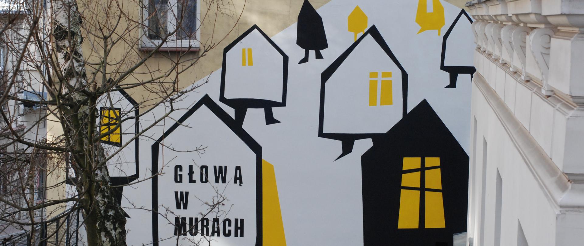 Mural przedstawiający stylizowane domy w kolorach czerni, bieli i żółci. Kompozycja przypomina wzgórze z unoszącymi się domkami o geometrycznych kształtach i żółtych oknach. Na jednym z domów widnieje napis „Głową w murach”. Przed muralem znajdują się bezlistne drzewa i fragment podwórza miejskiego.