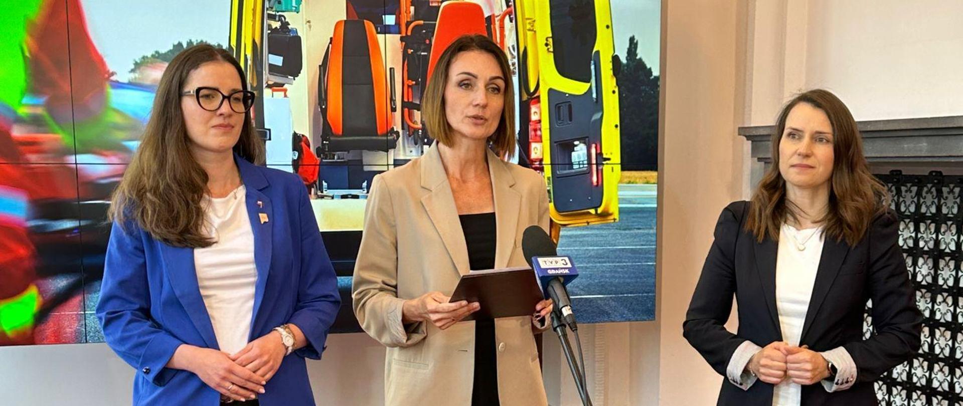 sala, na ekranie karetka pogotowia, przed mikrofonem stoi wojewoda, obok niej dwie posłanki