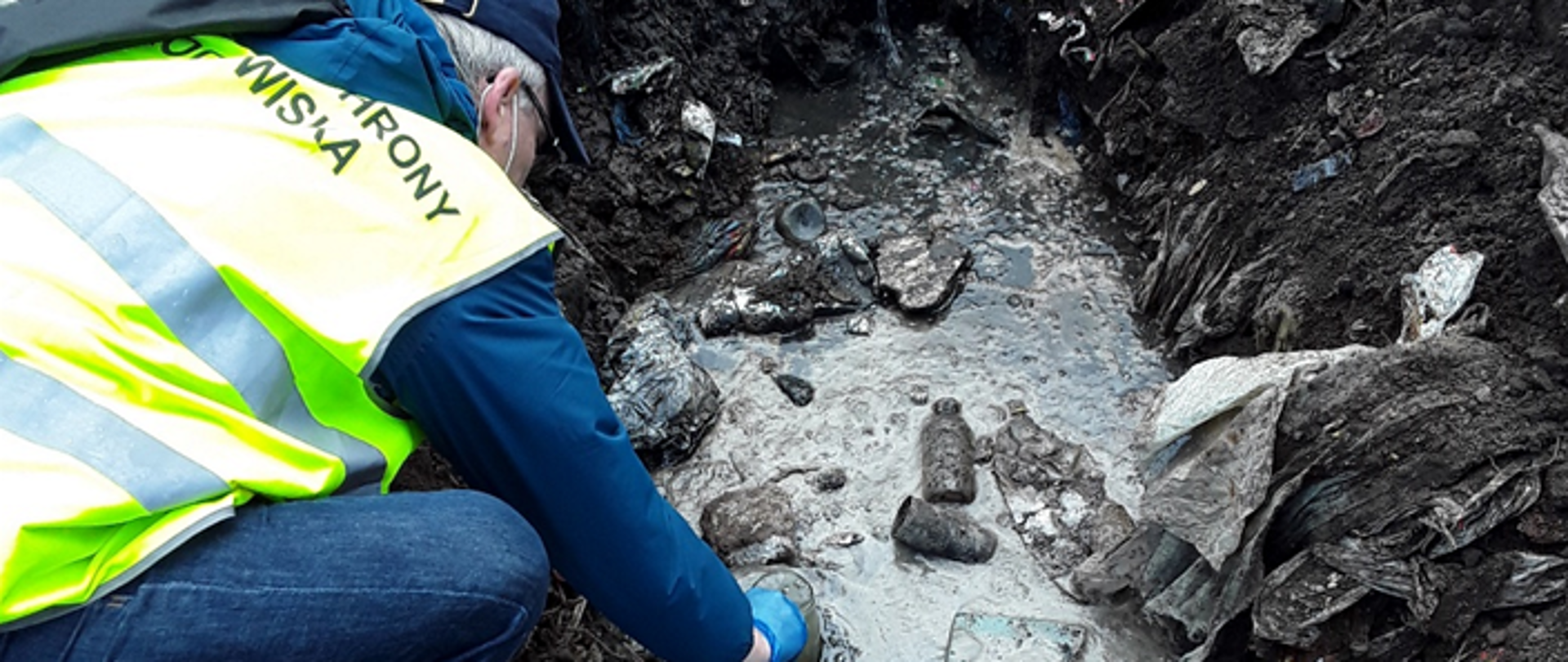 Mężczyzna kuca przy wykopie i zanurza naczynie w cieczy