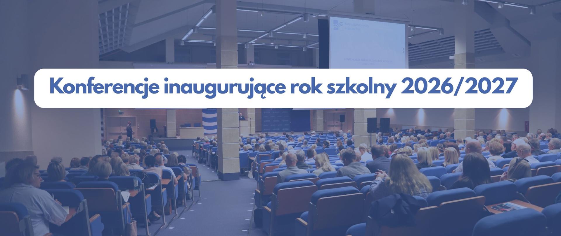 Uczestnicy konferencji inaugurującej siedzący w auli uniwersyteckiej, nad nimi projektor z prezentacją. Na zdjęciu znajduje się tekst: ,,Konferencje inaugurujące rok szkolny 2026/2027"/