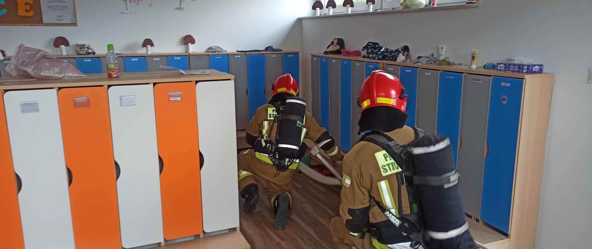 Rota strażaków wyposażona w sprzęt aparaty powietrzne z linią gaśniczą przeszukuje szatnie w żłobku.
