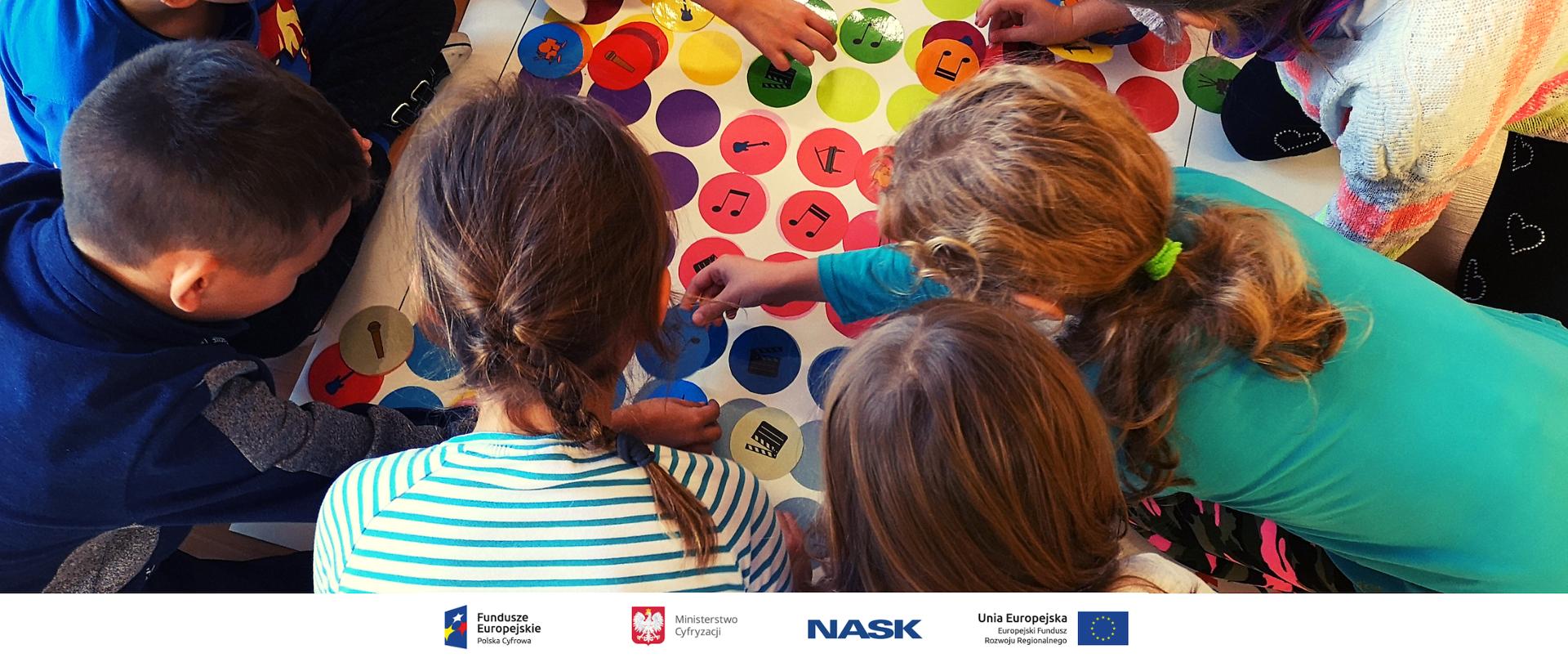 Na zdjęciu widać dzieci zajęte układaniem różnorodnych symboli związanych z muzyką na dużej planszy. U dołu znajduje się pasek logotypów: Europejskie Fundusze Polska Cyfrowa, Ministerstwo Cyfryzacji, NASK i Unia Europejska Europejski Fundusz Rozwoju Regionalnego.