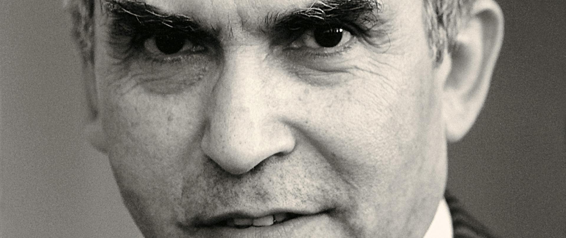 Adam Daniel Rotfeld czarno - biały portret mężczyzny, siwe włosy, ciemne brwi, szara marynarka w kratkę, ciemny krawat, biała koszula.