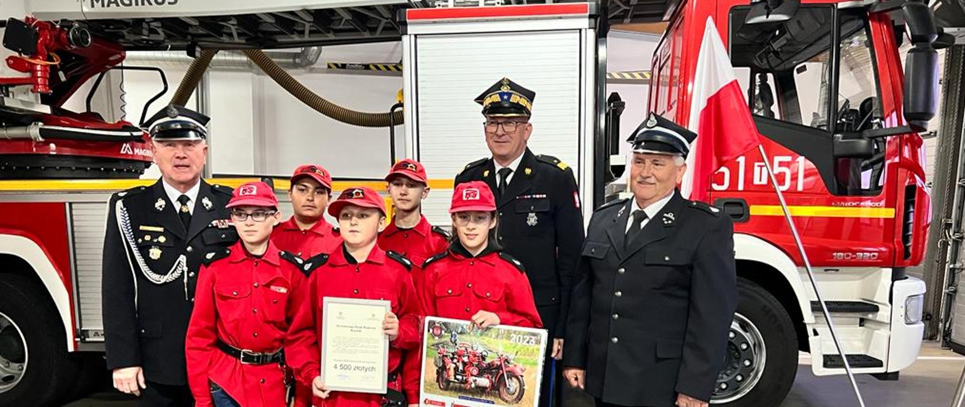 Zastępca KG PSP wraz z dziećmi z MDP oraz innymi uczestnikami zbiórki pozują do zdjęcia grupowego na tle samochodów rat. - gaś.