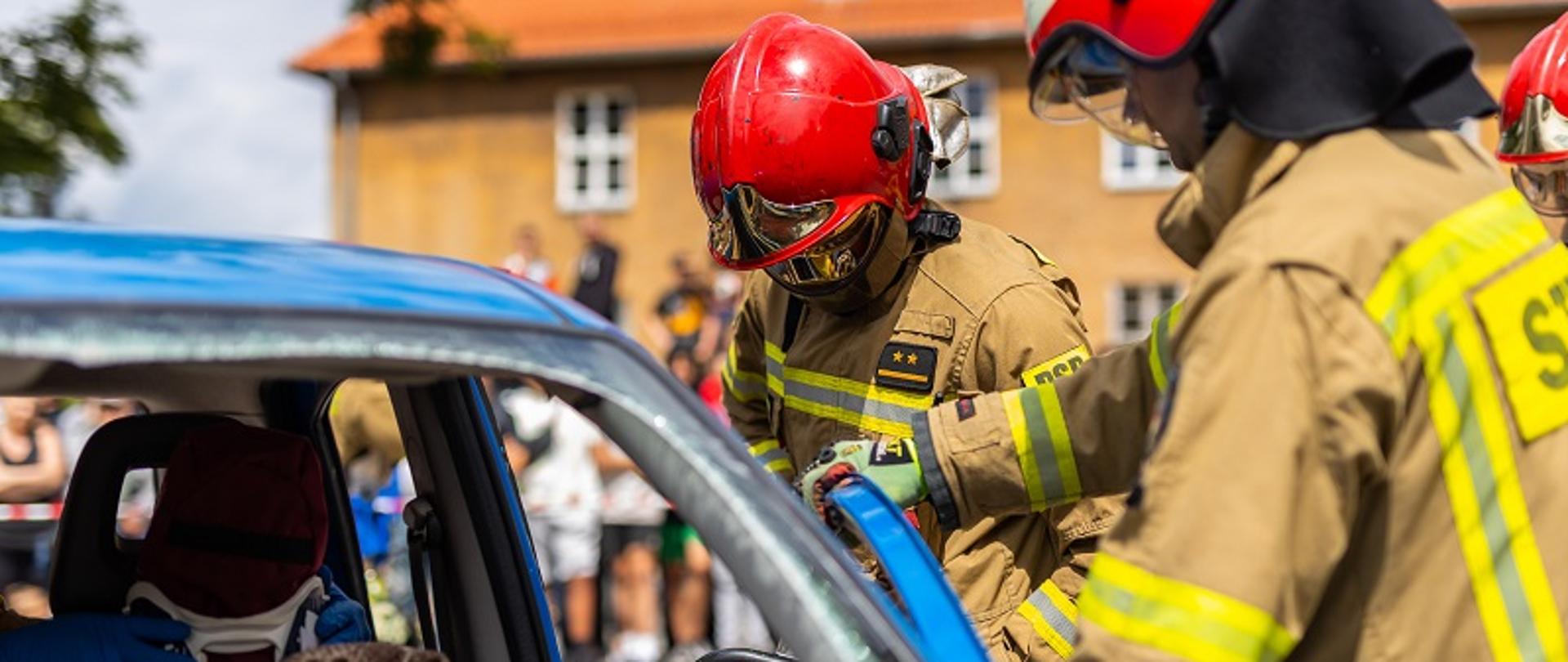 Zdjęcie przedstawia strażaków usuwających drzwi pojazdu