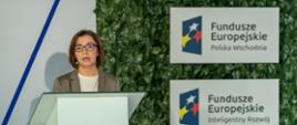 przy mównicy Małgorzata Wierzbicka, Dyrektor Departamentu Programów Ponadregionalnych, na ścianie logotypy programów Polska Wschodnia i Inteligentny Rozwój