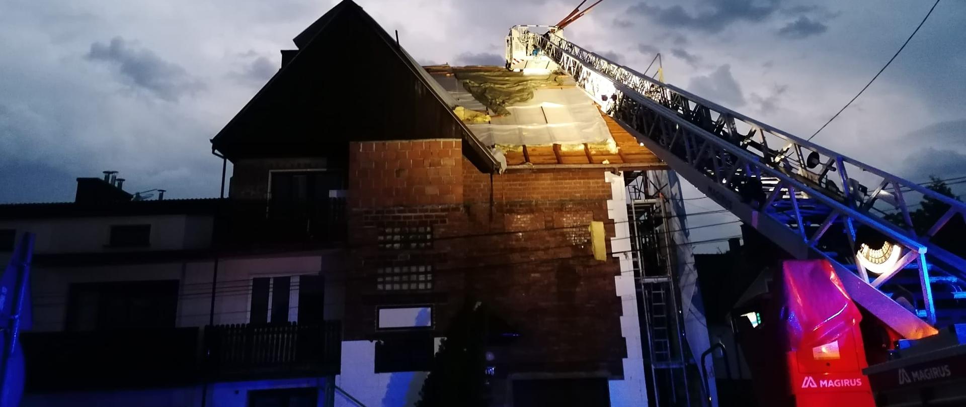 Zerwany dach na budynku mieszkalnym nocą, po prawej drabina mechaniczna