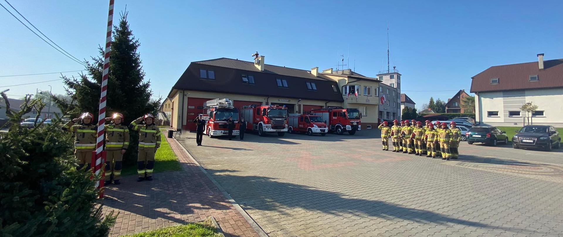 Panorama - na zdjęciu strażacy, strażnica oraz wozy bojowe wystawione przed strażnicą.