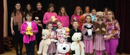 Zdjęcie przedstawia ubranych na różowo uczniów, stojących na scenie z pluszowymi misiami.