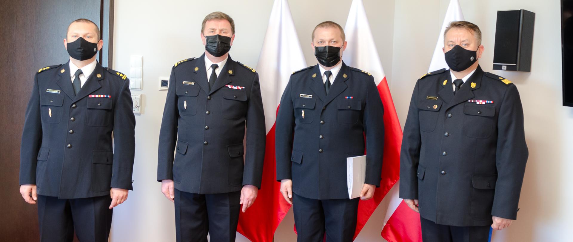 Począwszy od prawej strony stoją w mundurach galowych na tle flag państwowych:
- nadbryg. Jarosław Nowosielski – mazowiecki komendant wojewódzki PSP;
- bryg. Piotr Księżak – p.o. z-ca komendanta powiatowego PSP w Grodzisku Mazowieckim;
- st. bryg. Krzysztof Tryniszewski – komendant powiatowy PSP w Grodzisku Mazowieckim;
- bryg. Marcin Konecki – naczelnik Wydziału Kadr Komendy Wojewódzkiej PSP w Warszawie.
